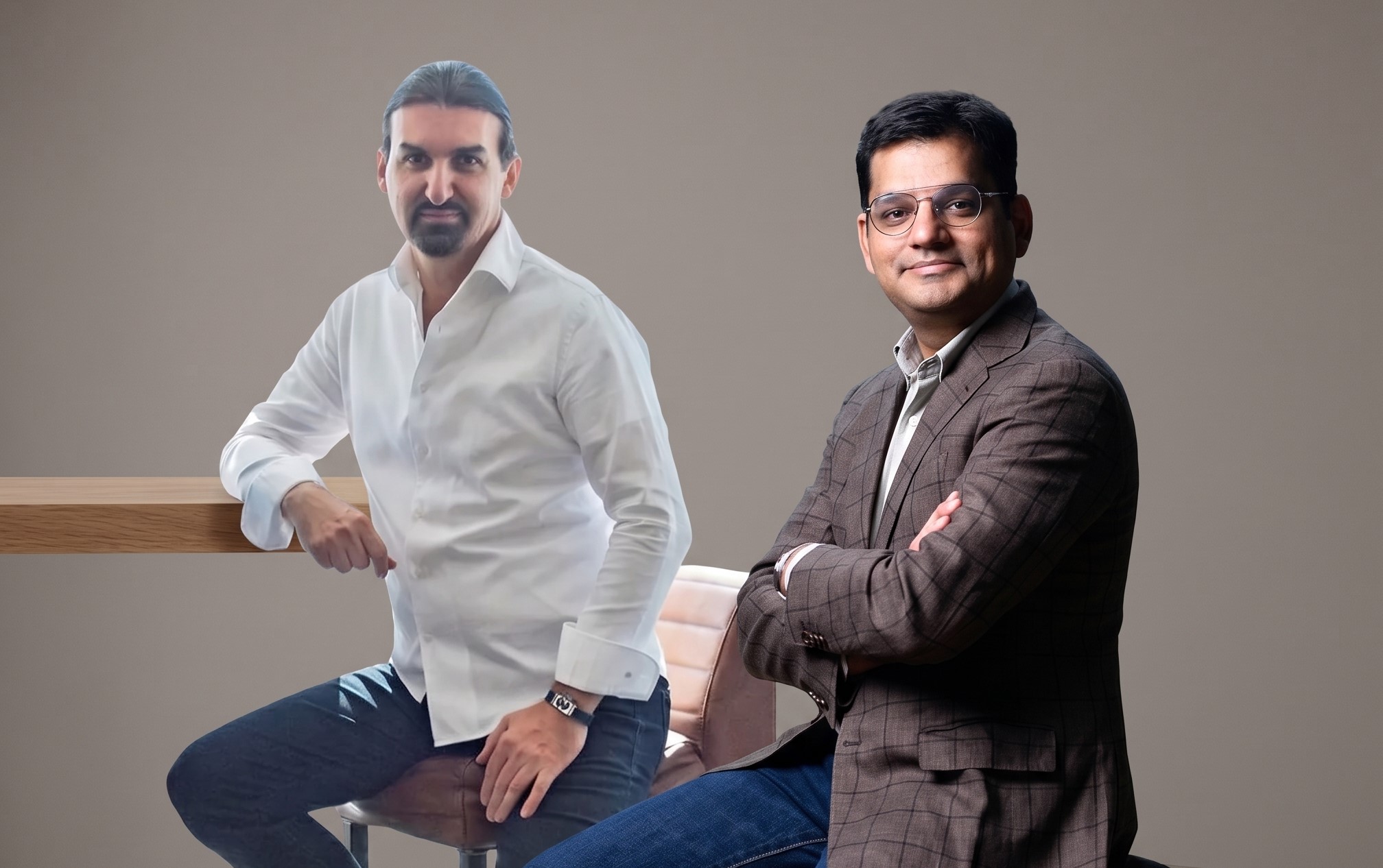Two men in professional attire pose for a photo, one seated and one beside a wooden table. Neutral background.